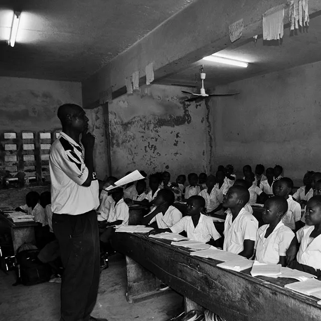 Guru SD menulis di papan tulis; siswa memperhatikan di kelas pedesaan Afrika